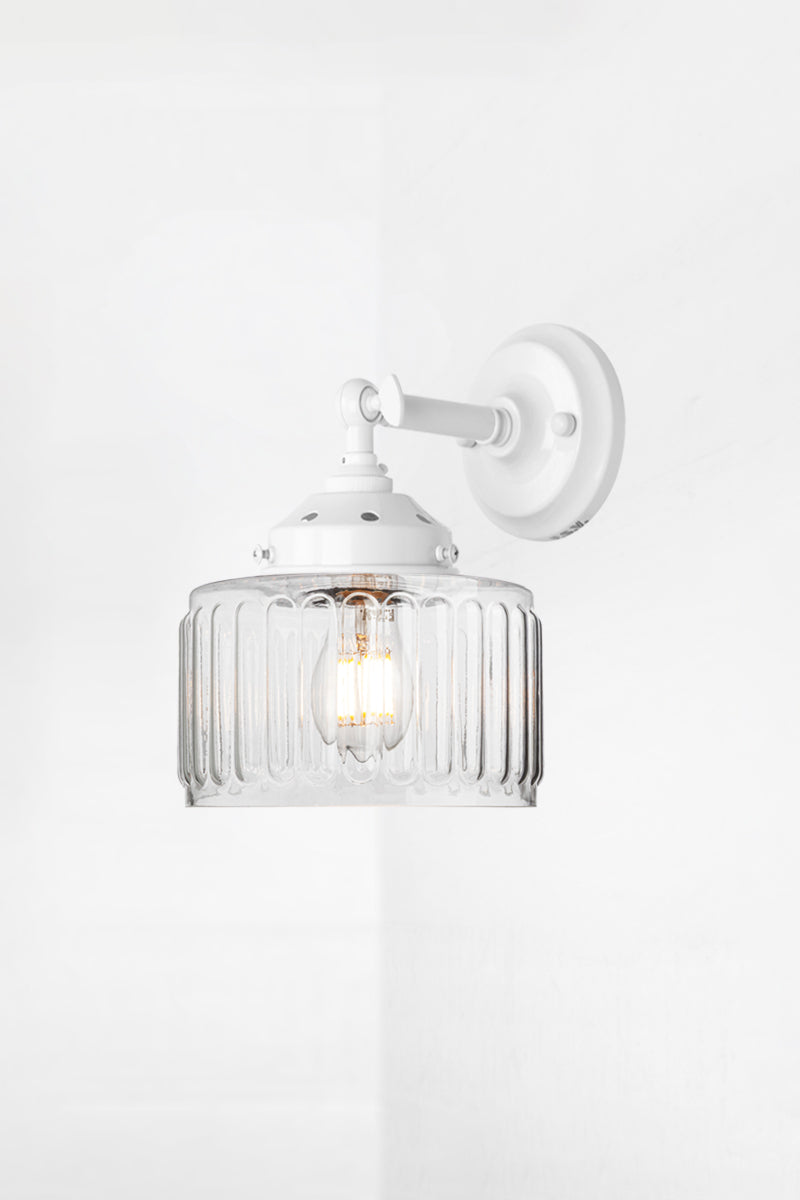 Clear glass shade with vintage fluted detailing on a short, white straight arm wall sconce with a swivel lampholder. 