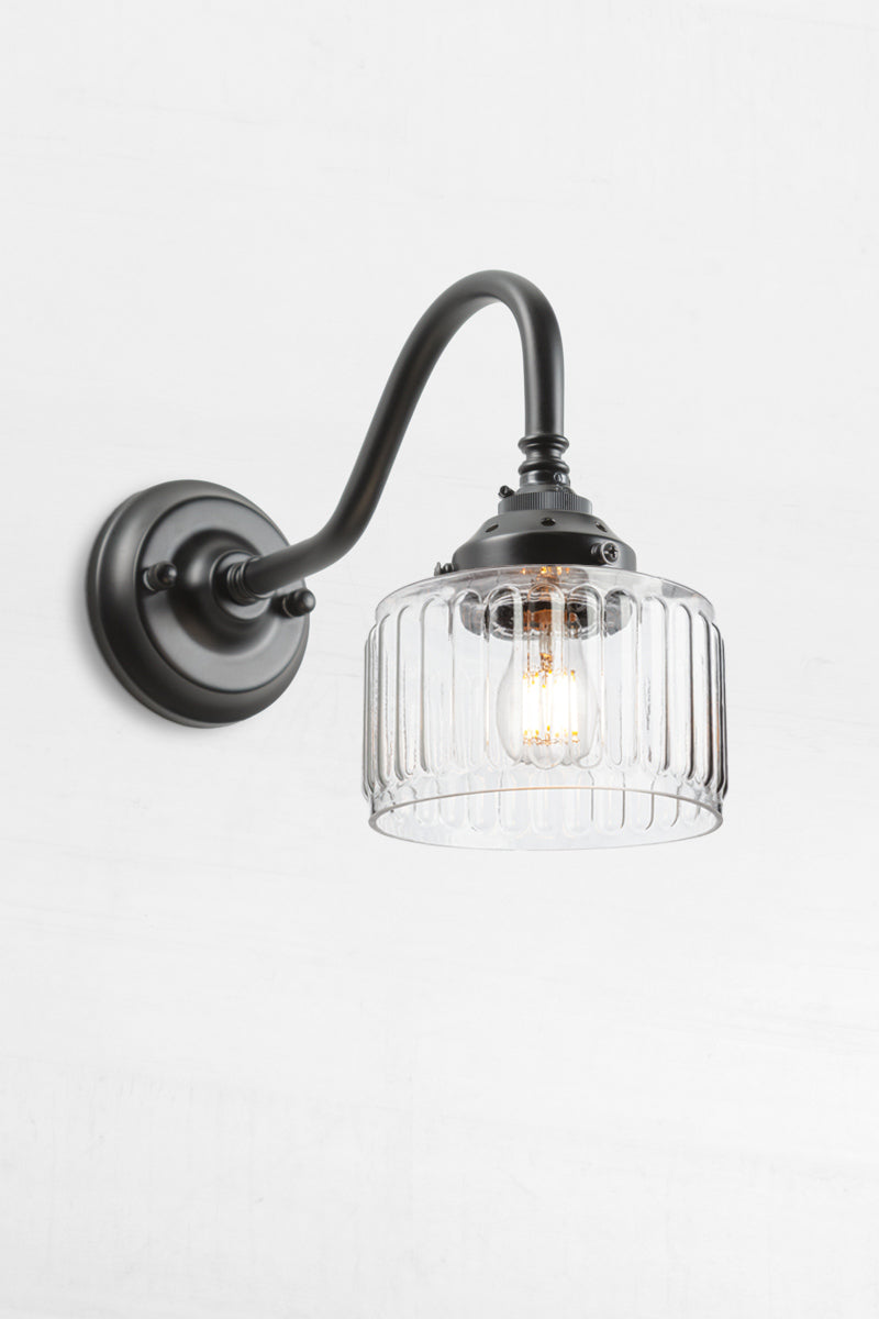 Clear glass shade with vintage fluted detailing on a black gooseneck wall sconce. 