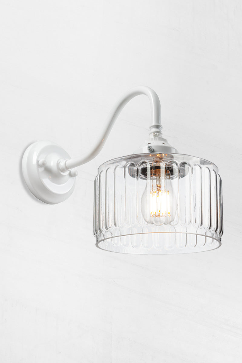 Clear glass shade with vintage fluted detailing on a white gooseneck wall sconce. 