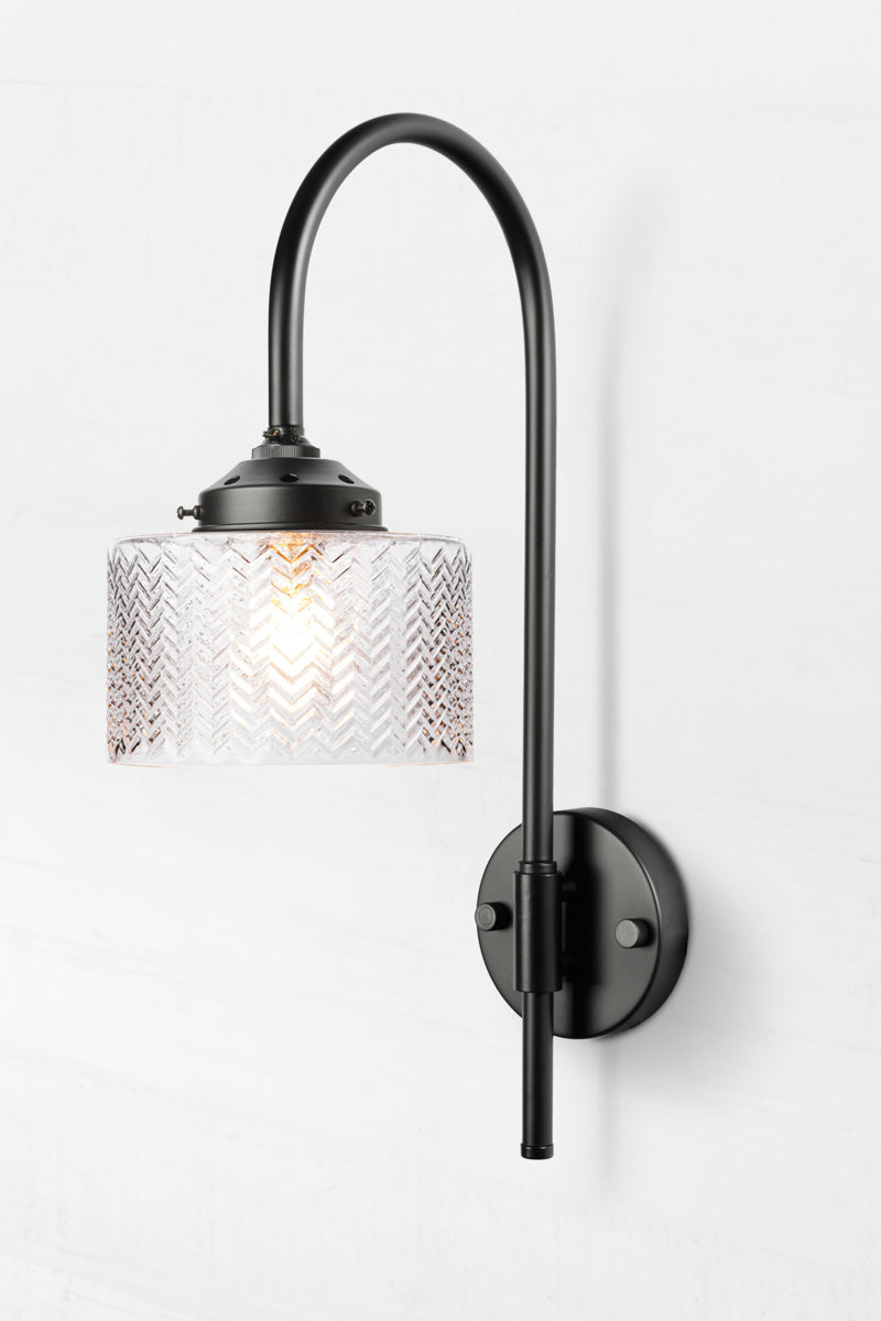 Black shepherds hook wall sconce paired with a clear glass shade with a wavy chevron detail. 