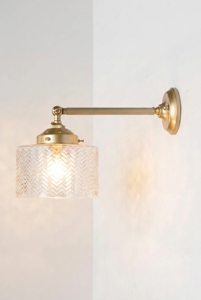 Illuminated Malibu Glass Swivel Wall Light with a long straight gold/brass arm , paired with a clear textured glass shade.