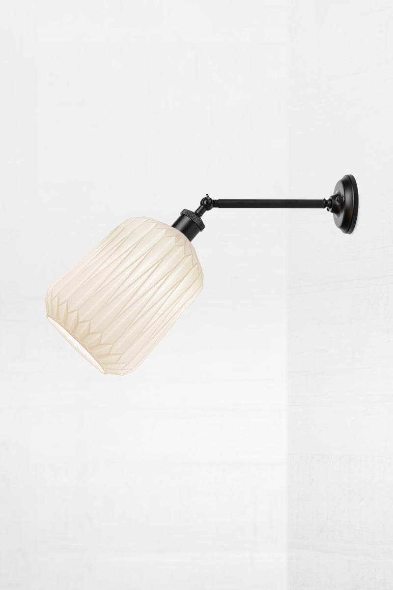 Wall sconce with a long black straight arm tilted out holding an opal glass shade with geometric detailing. 