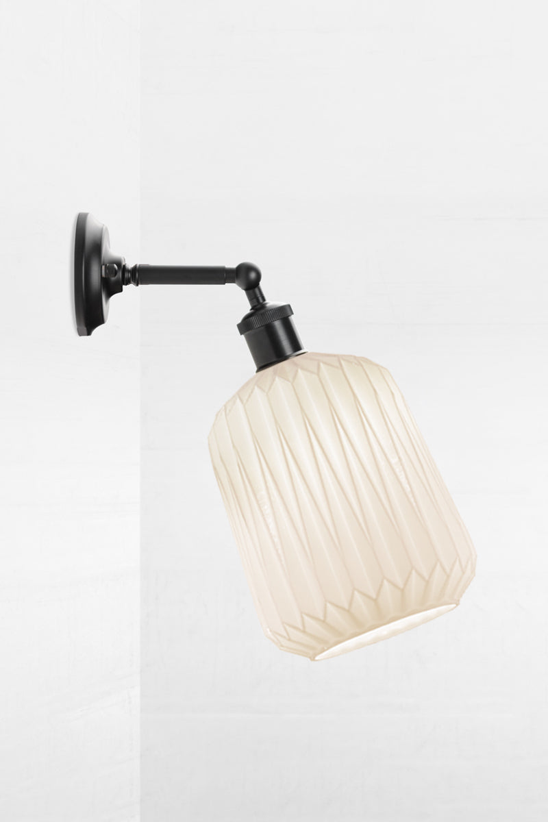 Wall sconce with a short black straight arm tilted out holding an opal glass shade with geometric detailing. 