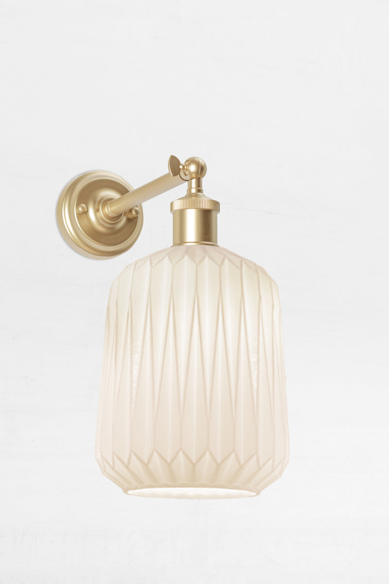 Wall sconce with a long gold/brass  straight arm tilted out holding an opal glass shade with geometric detailing. 