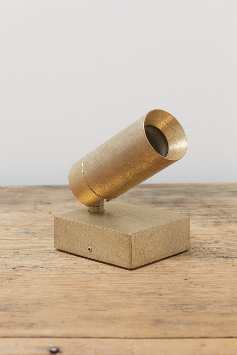 Antique brass adjustable wall spotlight displayed on a timber surface, showcasing the brushed brass finish and directional light head.