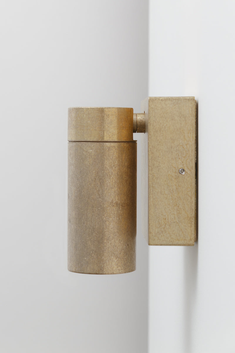 Side profile of an antique brass adjustable wall spotlight with cylindrical shade and square wall plate.