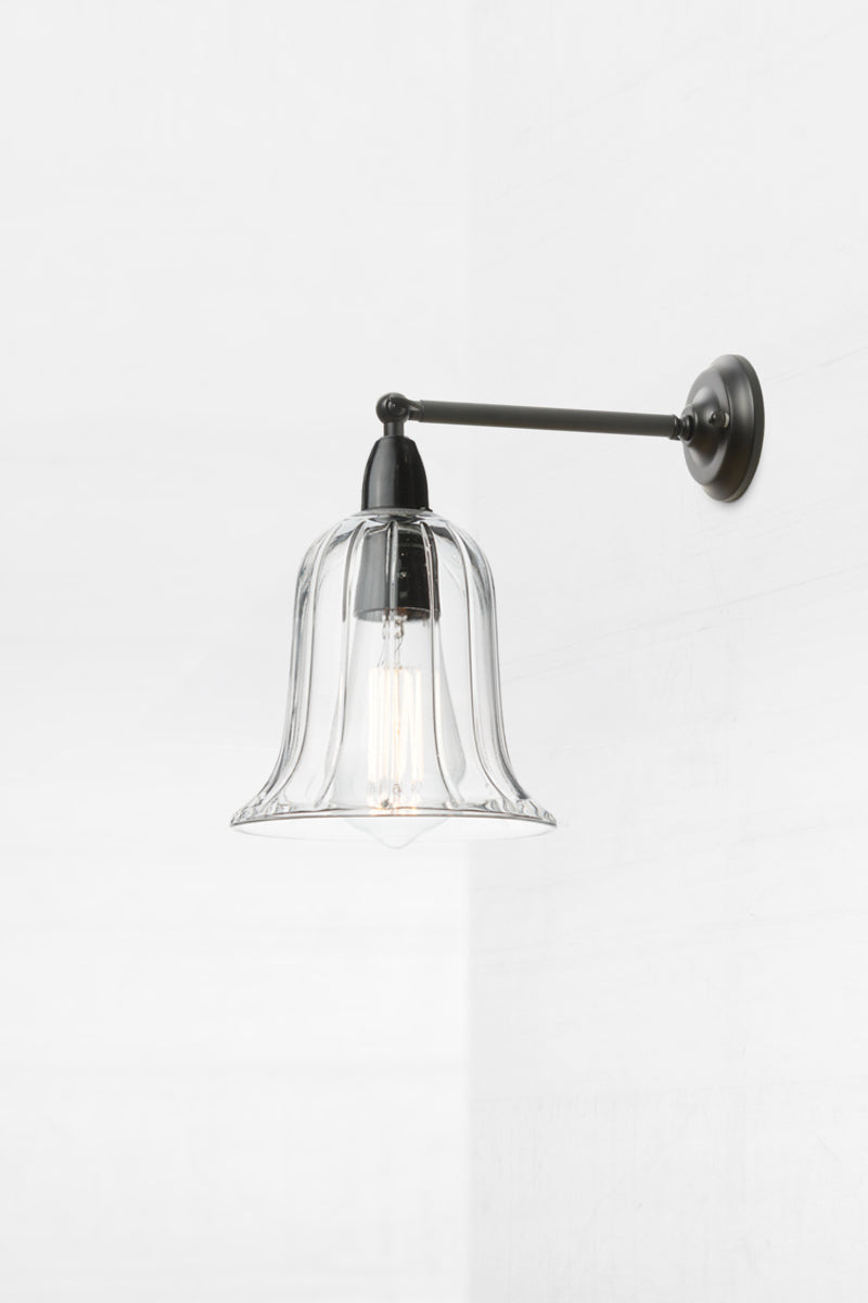 Bell shaped clear glass shade with subtle reeded detailing on an IP44 black exterior short, straight arm wall sconce. 