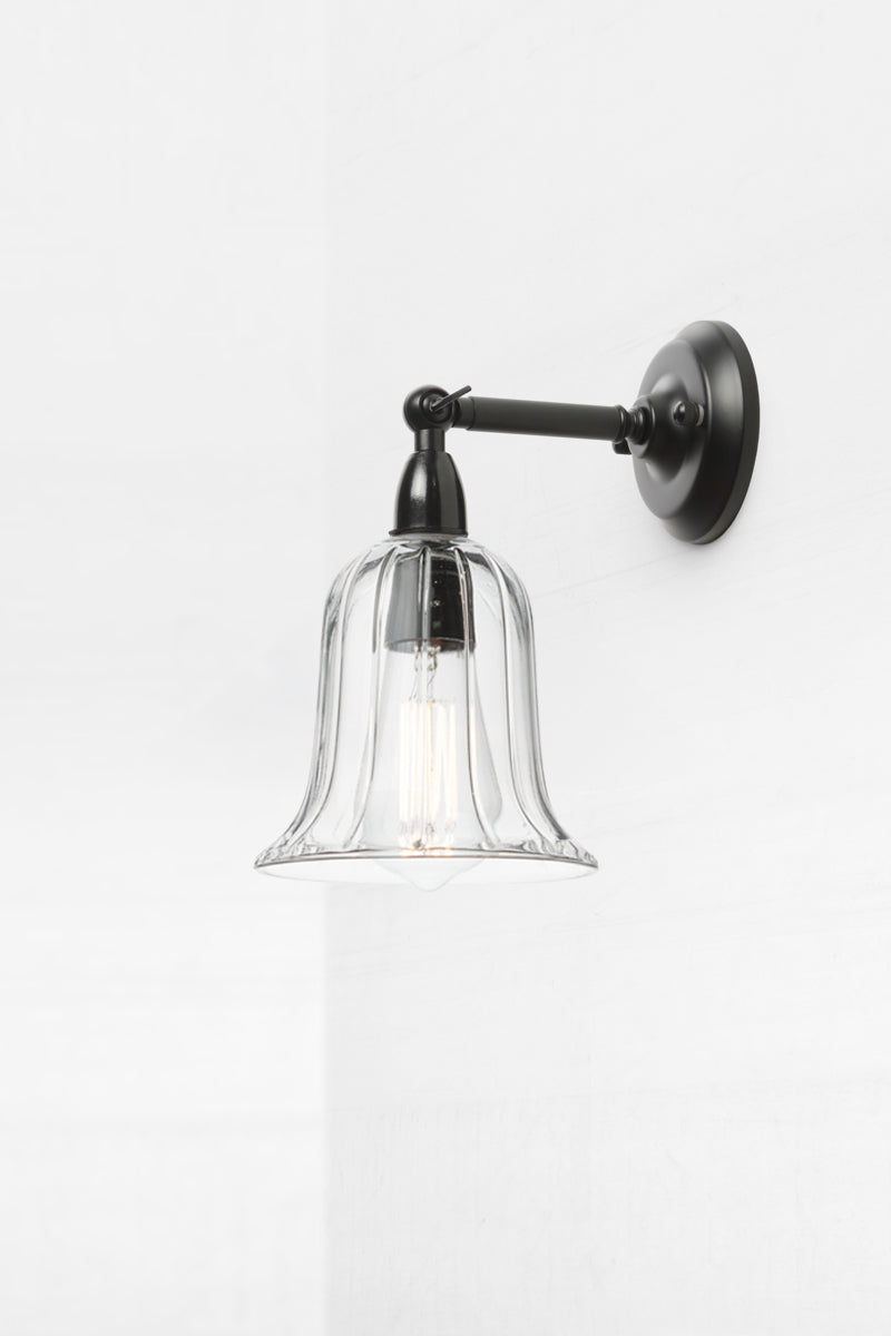 Bell shaped clear glass shade with subtle reeded detailing on an IP44 black exterior short, straight arm wall sconce. 