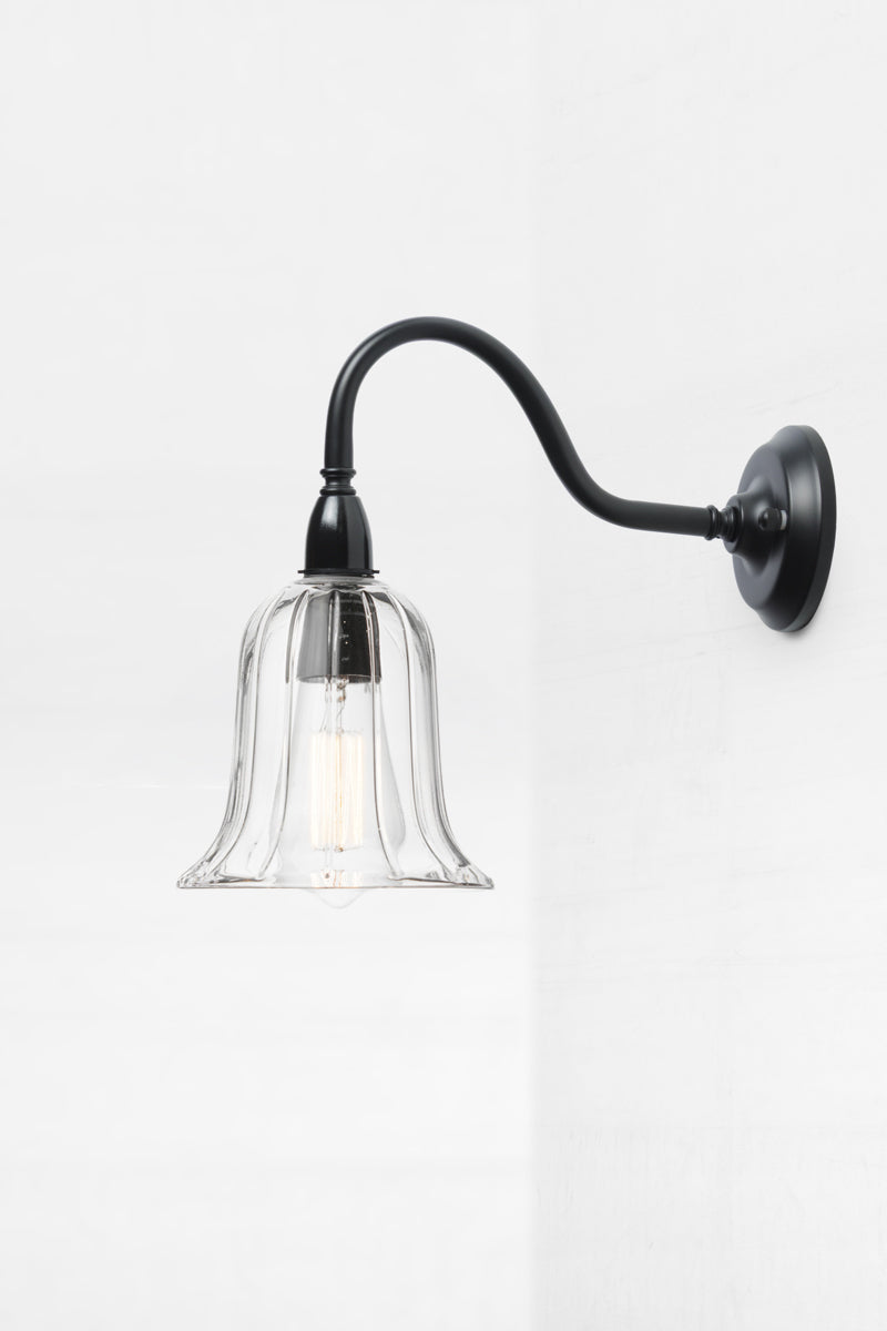 Side view of the bell shaped clear glass shade with subtle reeded detailing on an IP44 black exterior gooseneck wall sconce. 