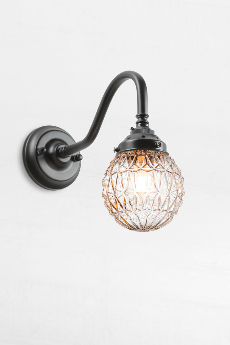 Glass ball shade with diamond cut detailing paired with a black gooseneck wall arm.