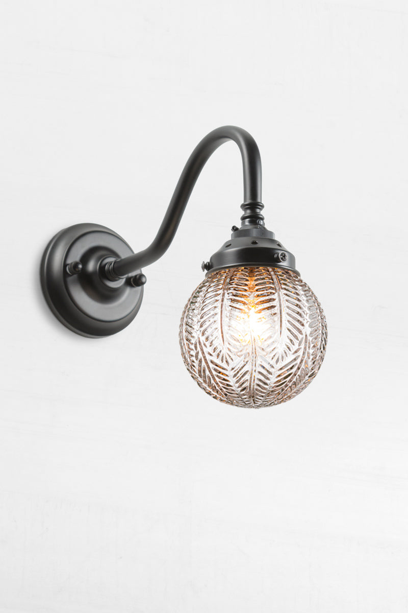 Gooseneck arm wall sconce in black with a clear glass orb shade with intricate detailing. 