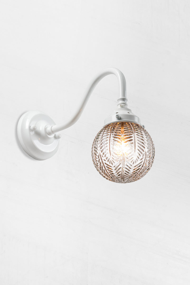 Gooseneck arm wall sconce in white with a clear glass orb shade with intricate detailing. 