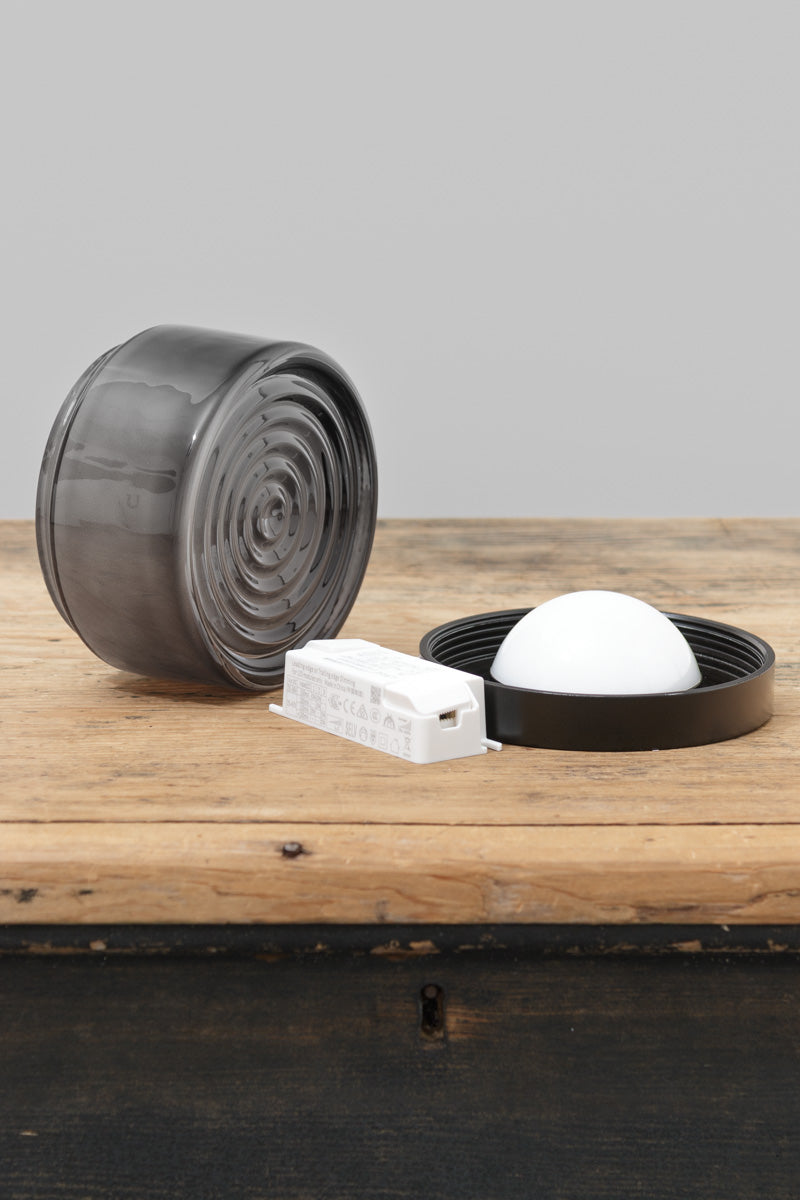 Grey LED glass wall light displayed on a timber surface beside mounting components and LED driver.