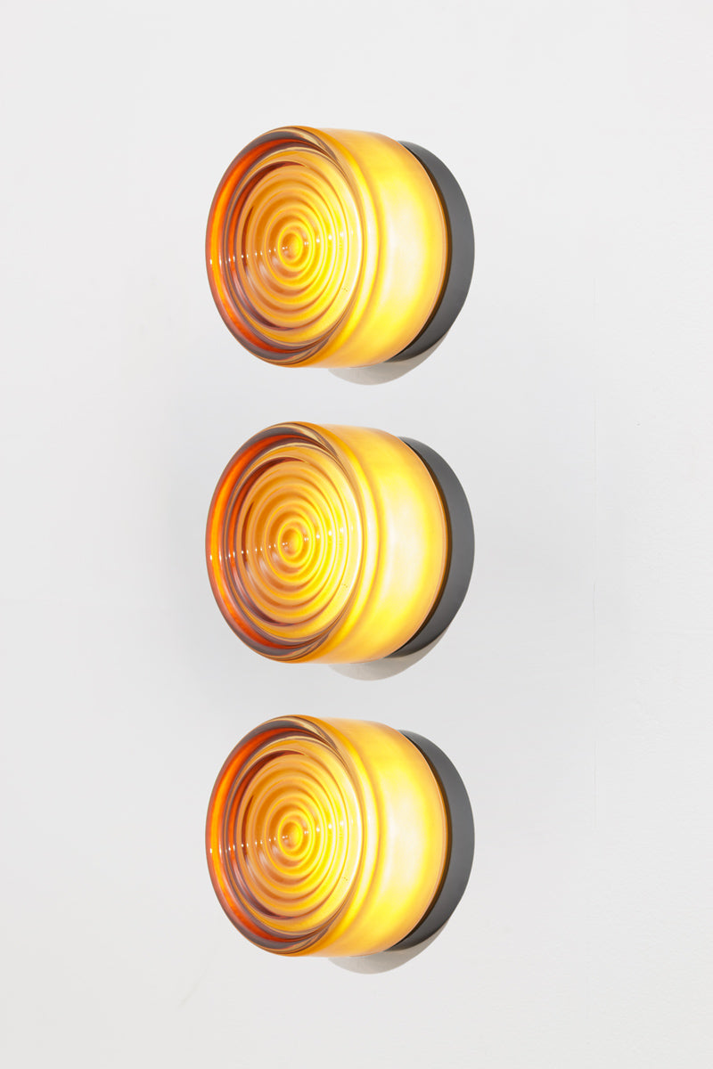 Side profile view of a bundle of three amber LED glass wall lights with glowing ribbed glass shades.