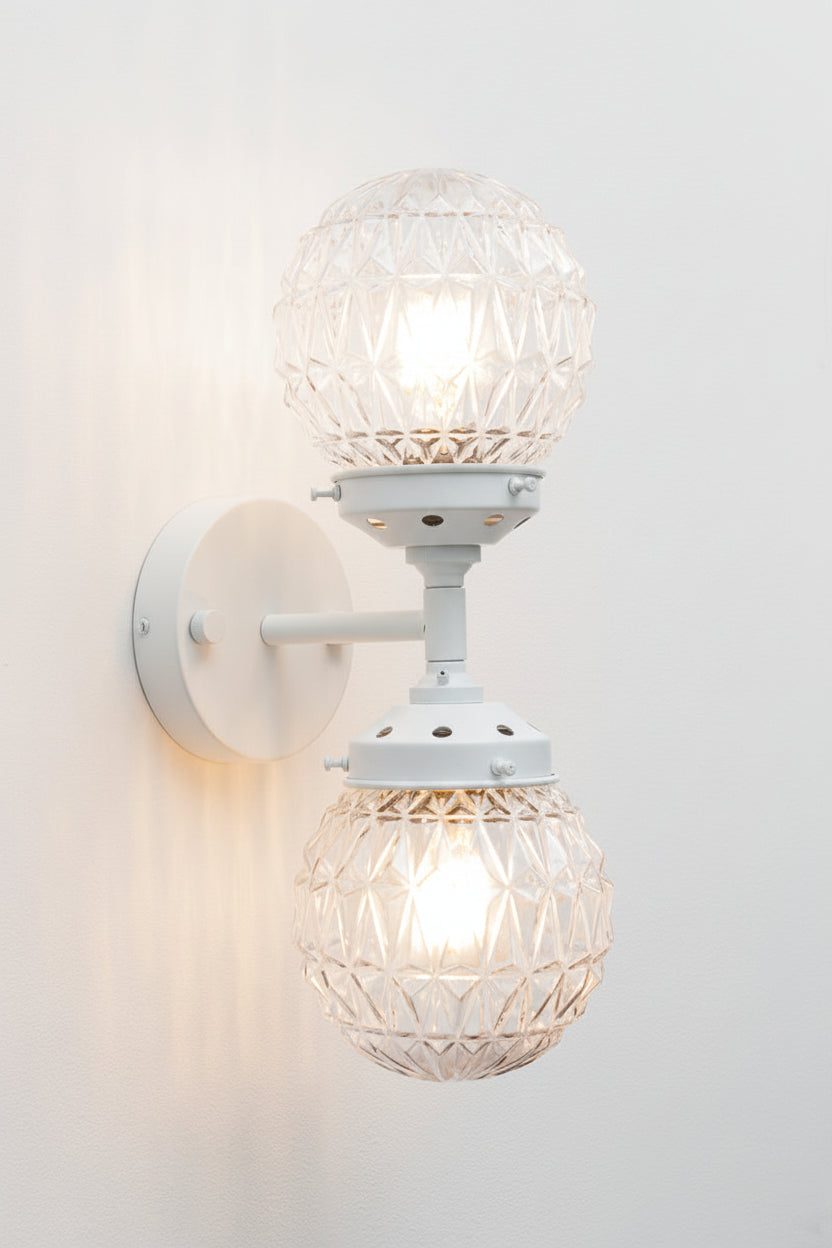 clear glass sphere with diamond cut points design on a white wall sconce with dual lampholders