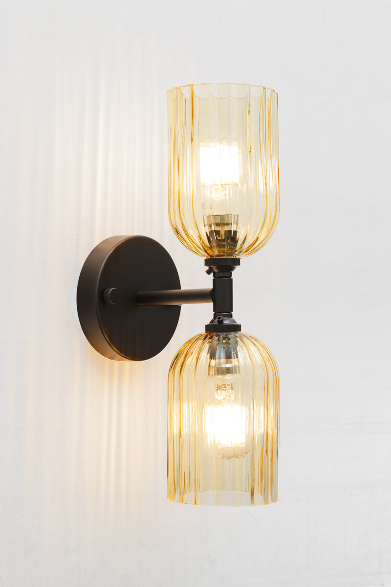 Black double wall sconce with two elongated amber glass shades with fluted detailing.