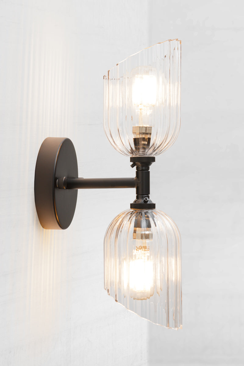 Black double wall sconce with two clear glass shades with fluted detailing and angled cut design. 
