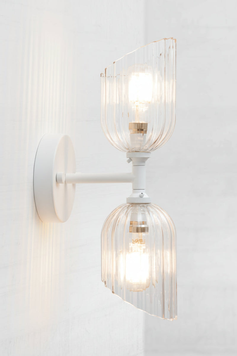 White double wall sconce paired with two eloganted clear glass fluted with reeded detailing and an angled cut. 
