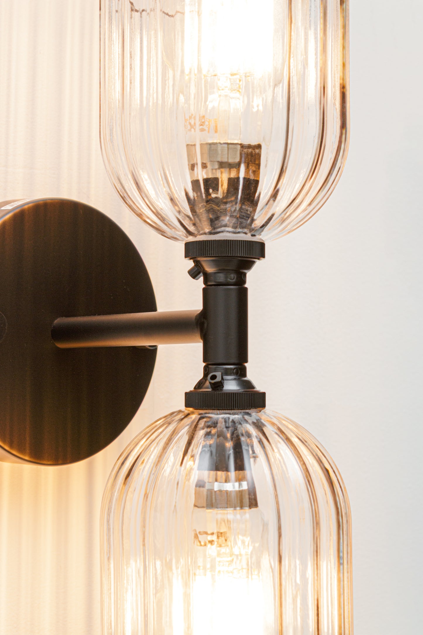 Close up of the black double wall sconce lampholders and two clear glass shades with fluted detailing.