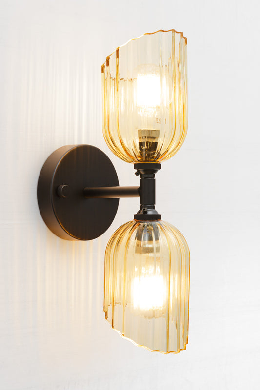 Black double wall sconce with two amber glass shades with fluted detailing and angled cut design. 