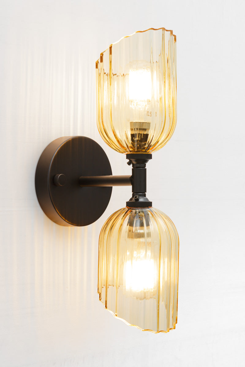 Black double wall sconce with two amber glass shades with fluted detailing and angled cut design. 