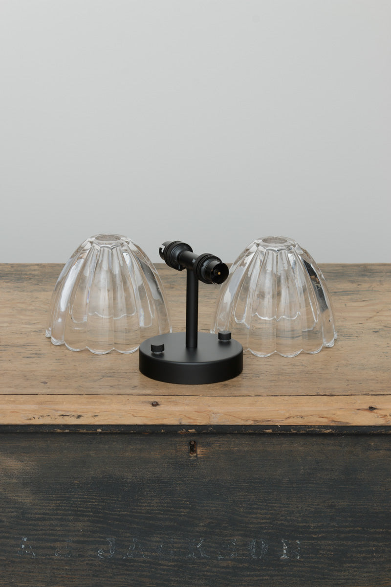 Uninstalled wall light with a black fixture and two lear glass shades on a timber trunk.