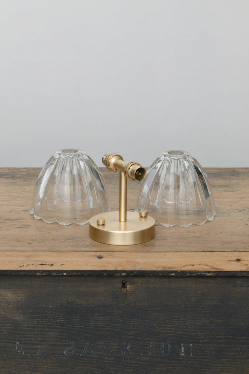 Uninstalled wall light with a gold/ brass fixture and two lear glass shades on a timber trunk.