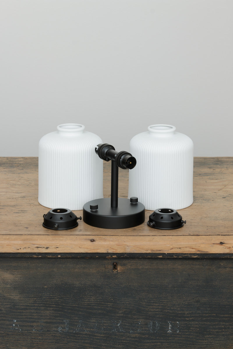 Two matt white ceramic shades with reeded detailing, black sconce and galleries uninstalled on a timber trunk. 
