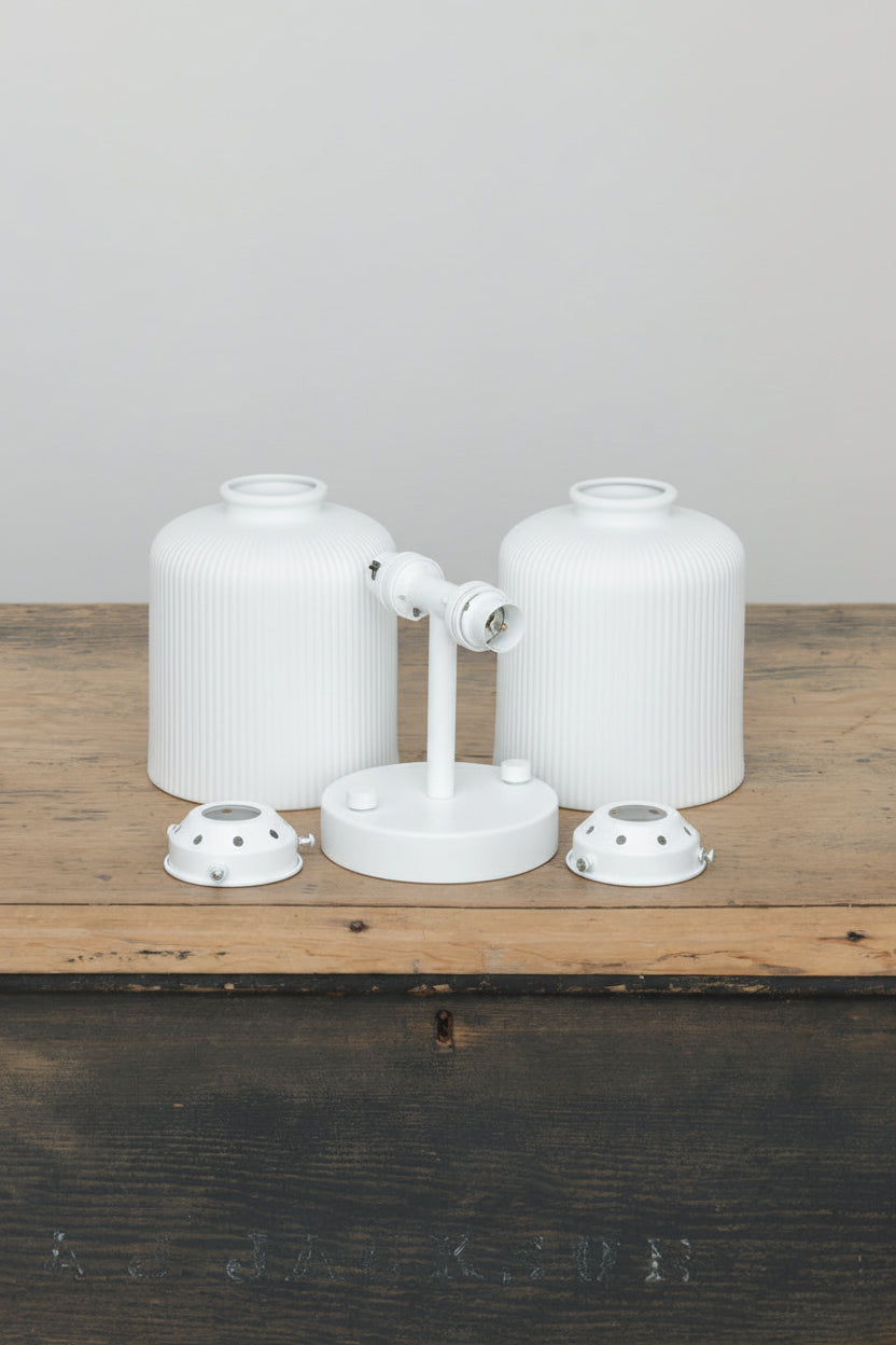 Two matt white ceramic shades with reeded detailing, white sonce and galleries uninstalled on a timber trunk. 