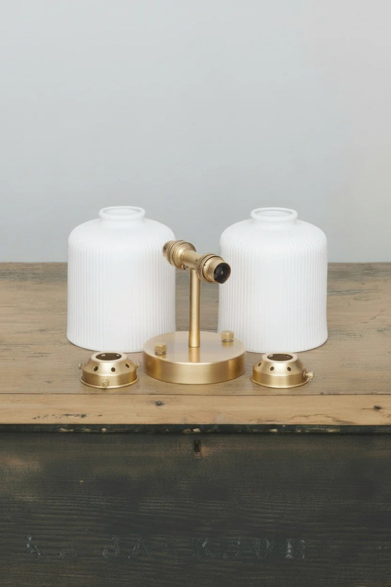 Two matt white ceramic shades with reeded detailing, gold/brass sconce and galleries uninstalled on a timber trunk. 