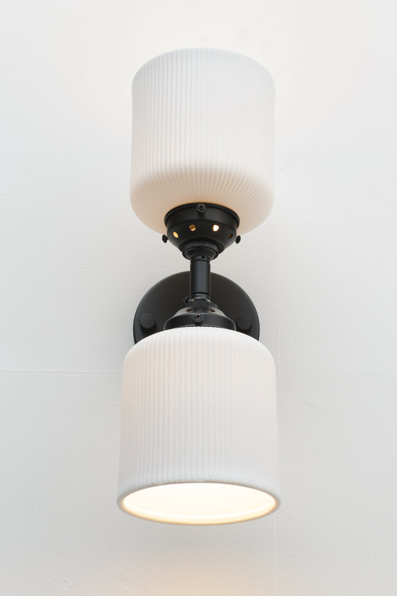 Front view of the black double wall sconce fixture paired with two unglazed white ceramic shades. 