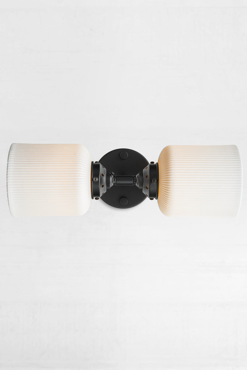 Black double wall sconce fixture paired with two unglazed white ceramic shades installed sideways