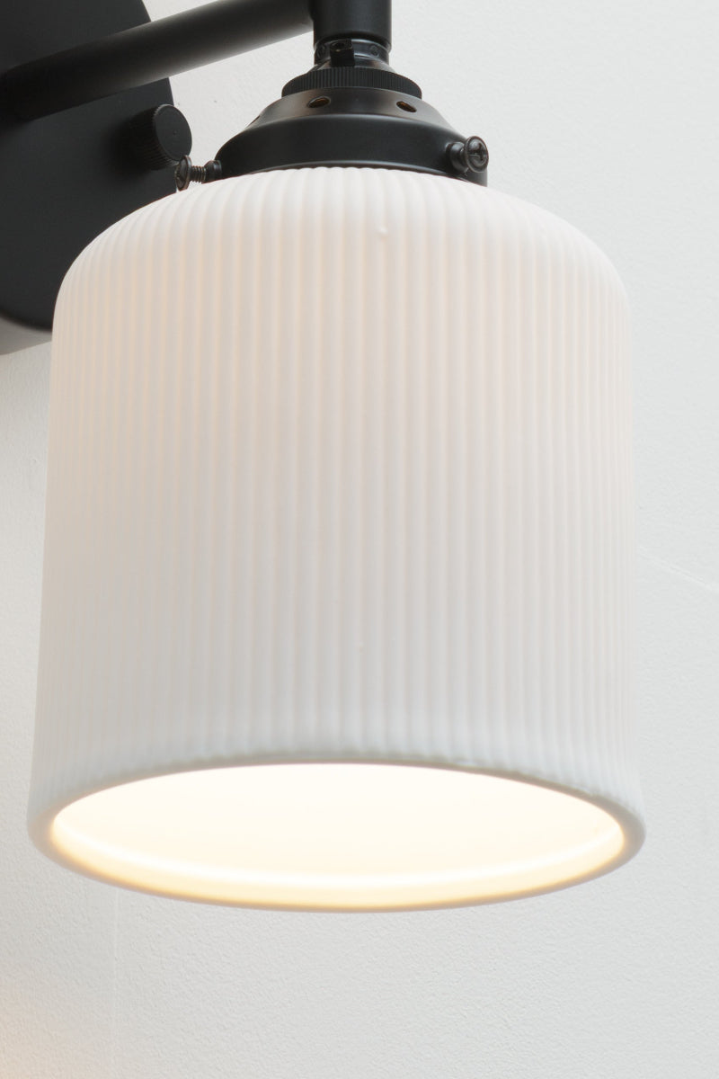 Wall sconce fixture with a black sconce paired with two unglazed white ceramic shades. 