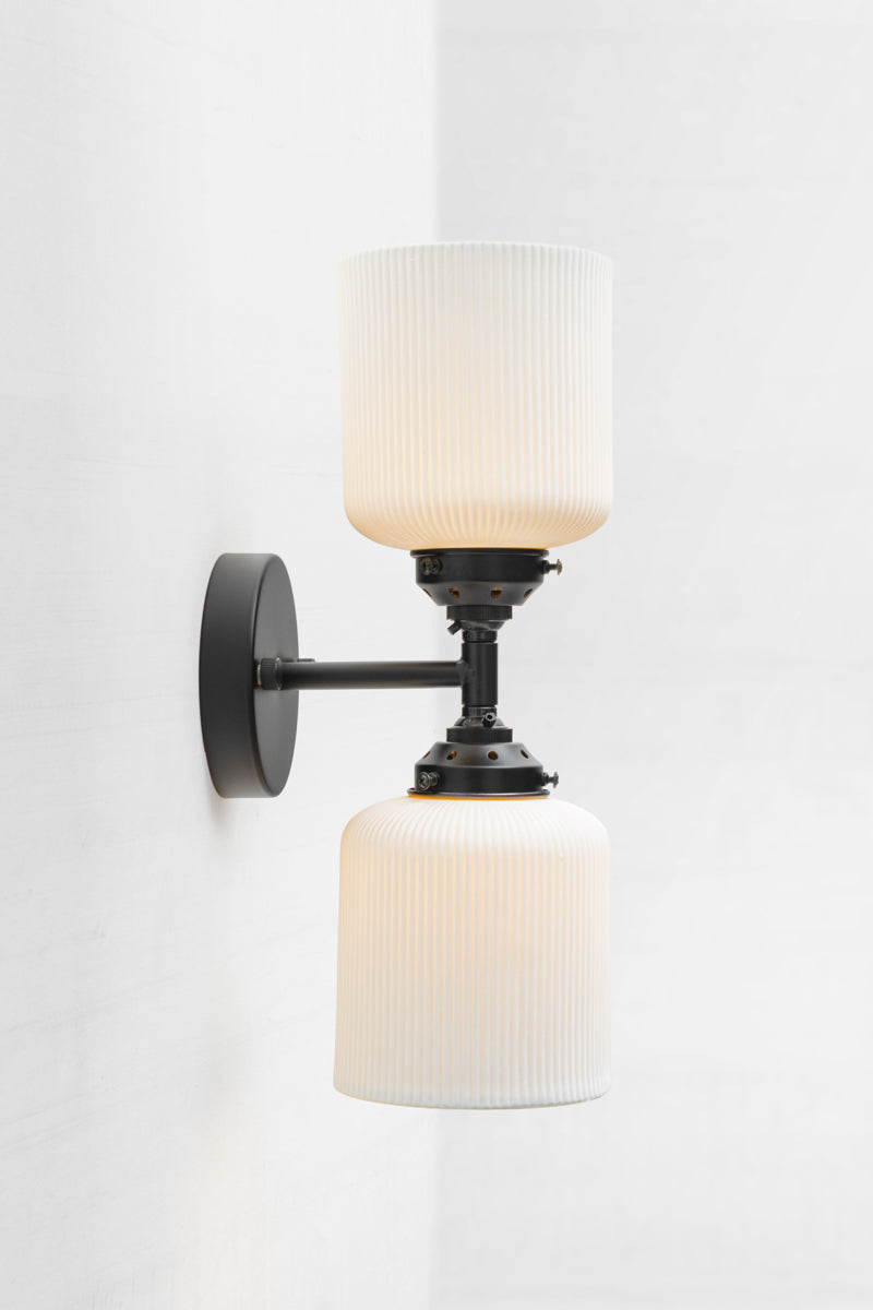 Side view the black double wall sconce fixture paired with two unglazed white ceramic shades. 