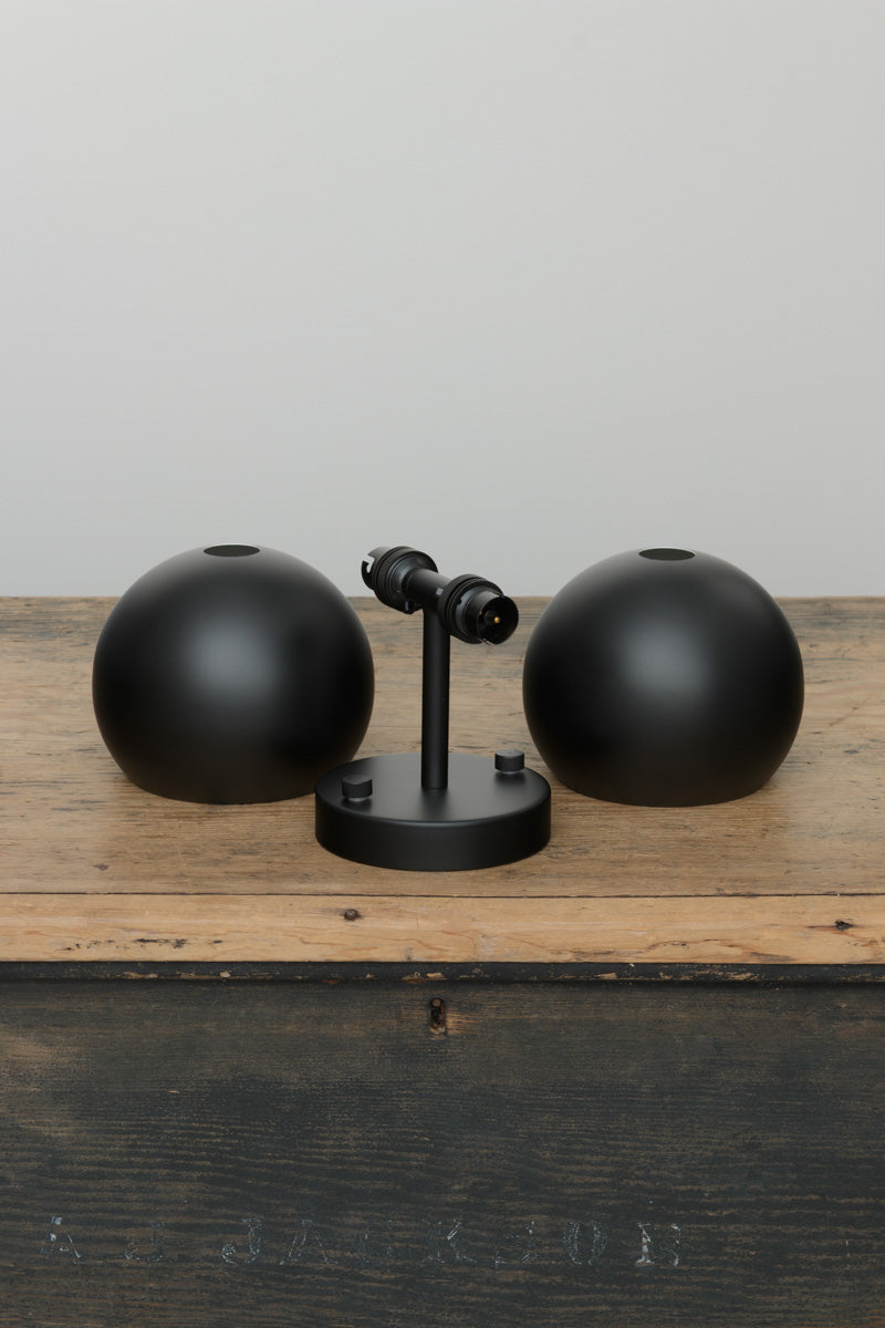 Uninstalled black double wall sconce with two steel bulb shades in black on a timber trunk image. 