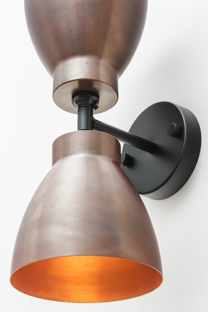 Close up of the black double wall sconce with two solid copper bell-shaped shades. 