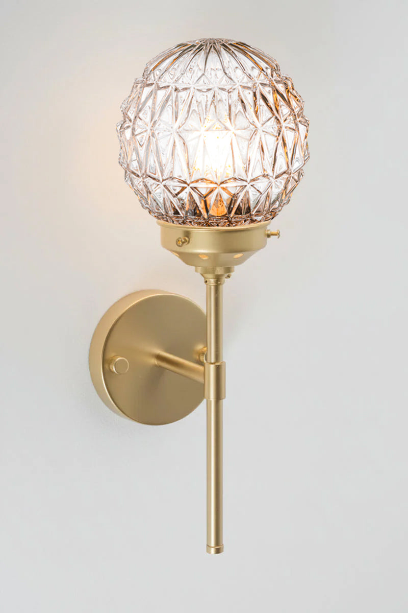 Clear glass ball shades with diamon-cut detailing paired with a gold/brass steel stem wall sconce. 
