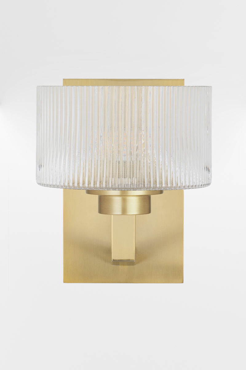 Front view of the wall sconce in Antique Gold with a rectangular mount plate and arm, holding a clear reeded cylindrical glass shade.