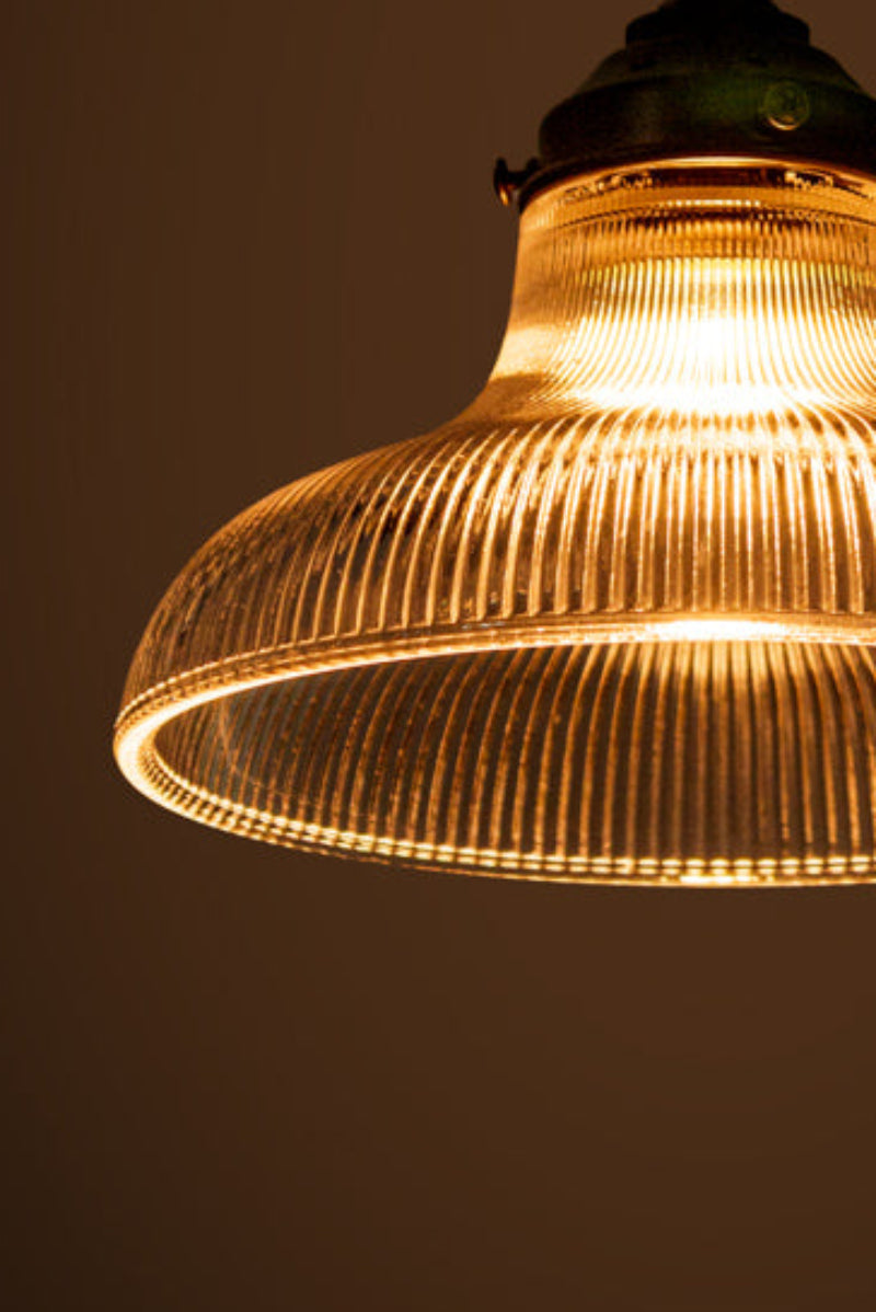 Small clear holohpane glass shade illuminated in a dark room. 