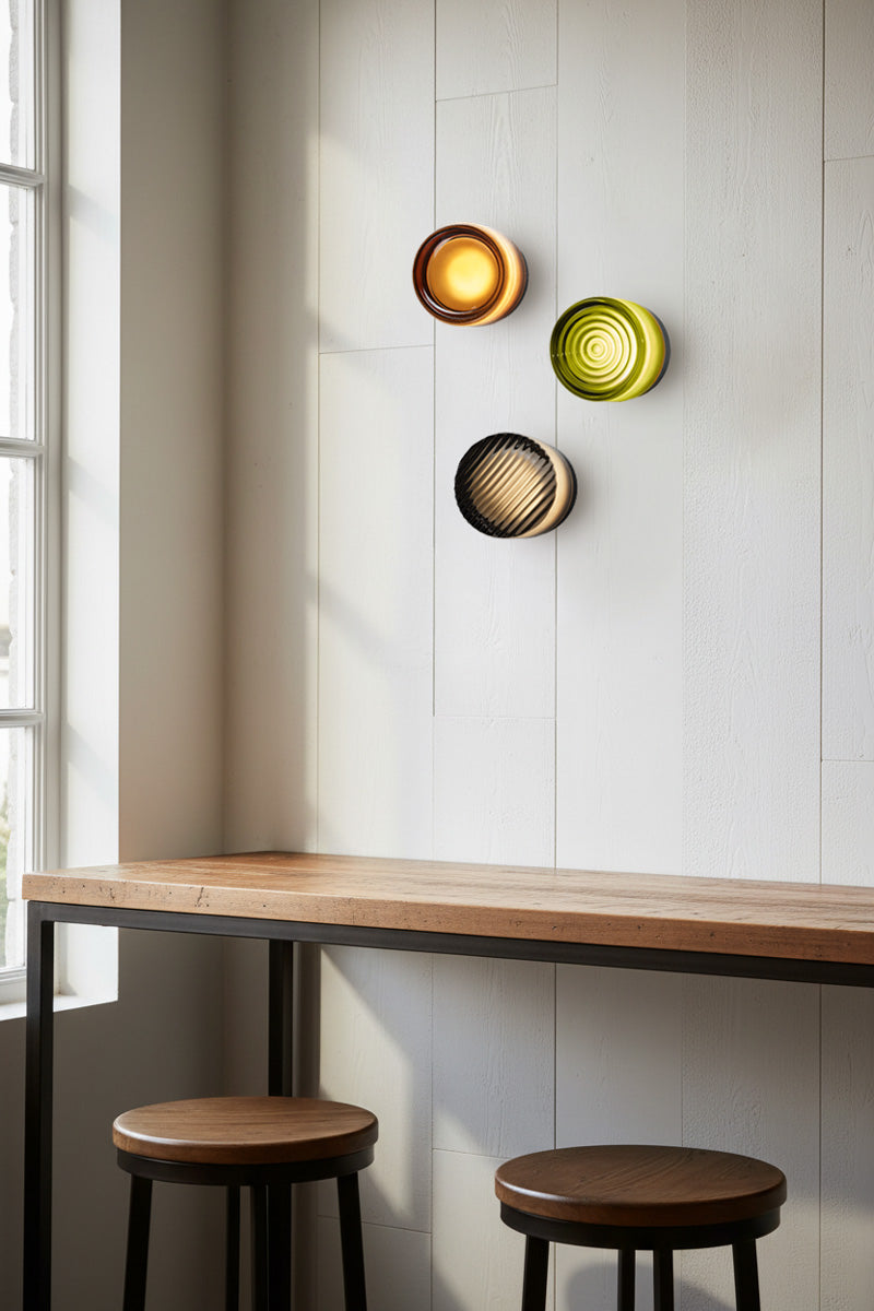 Modern wall lights with sage, amber, and grey shades on a white wall above a bar wooden table. 