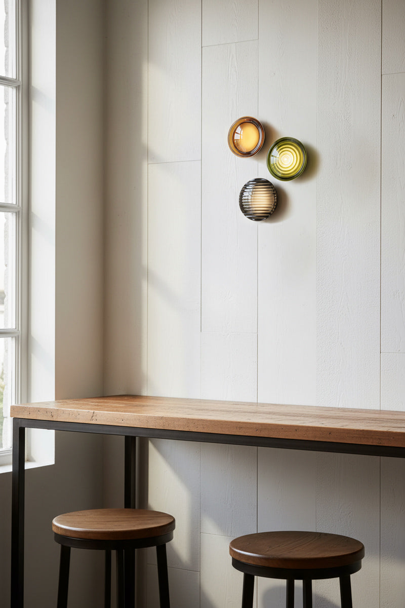 Modern interior with wooden bar counter and stools against a light tiled wall with 3 decorative glass wall lights.