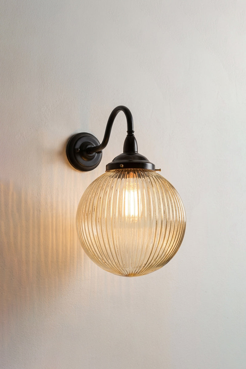 Illuminated medium amber reeded glass ball shade on a large gooseneck outdoor wall arm in black. 