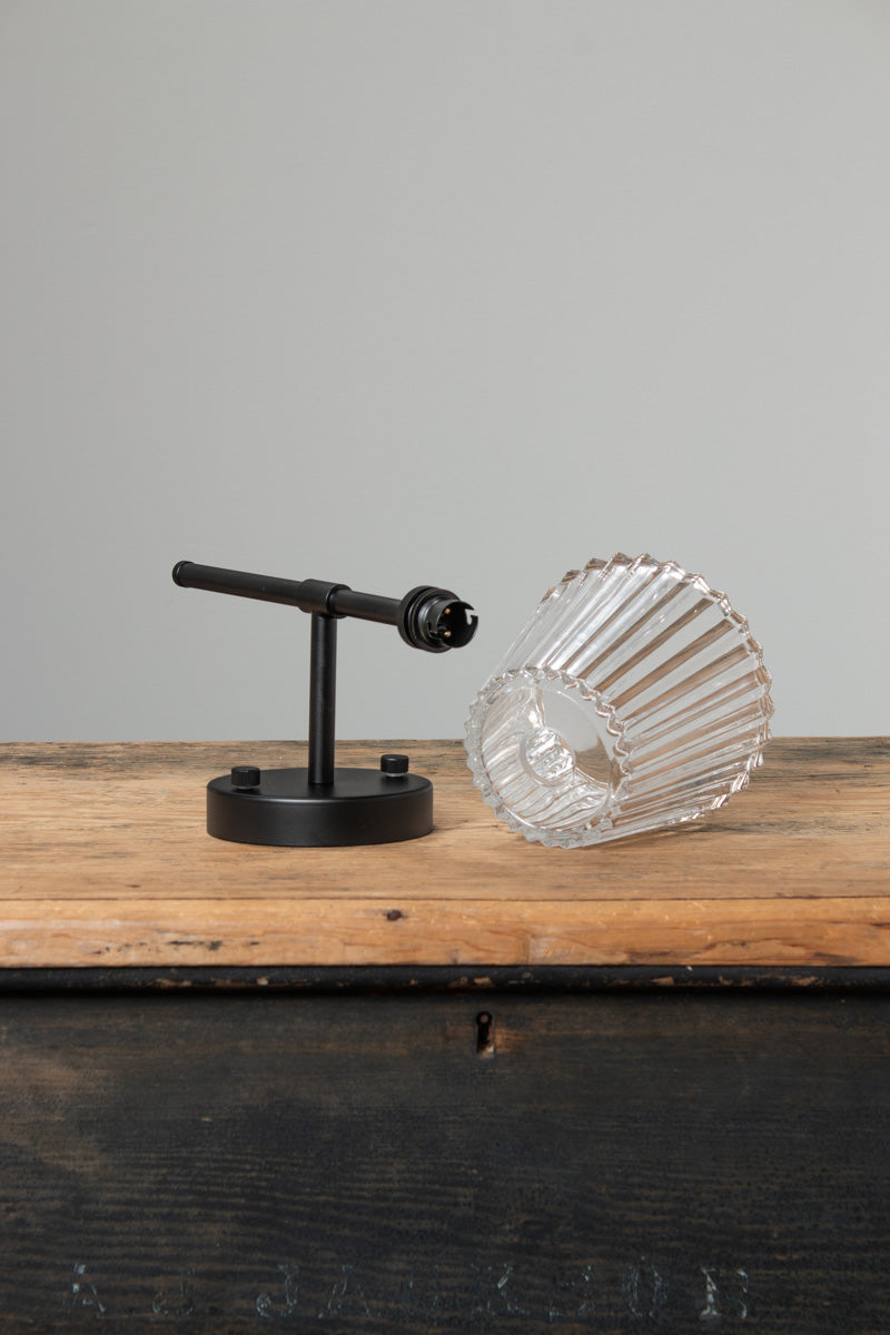 Black Davis Glass Stem Wall Light displayed with clear fluted glass shade on timber surface.