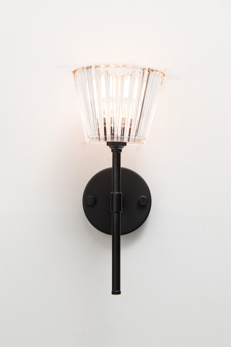 Front view of black Davis Glass Stem Wall Light illuminated against a white wall.