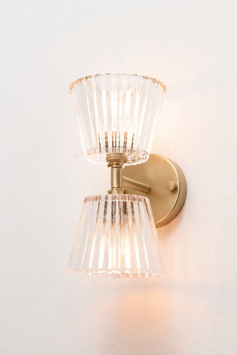 Angled view of gold/brass Davis Glass Double Light Wall Sconce with two illuminated clear glass shades