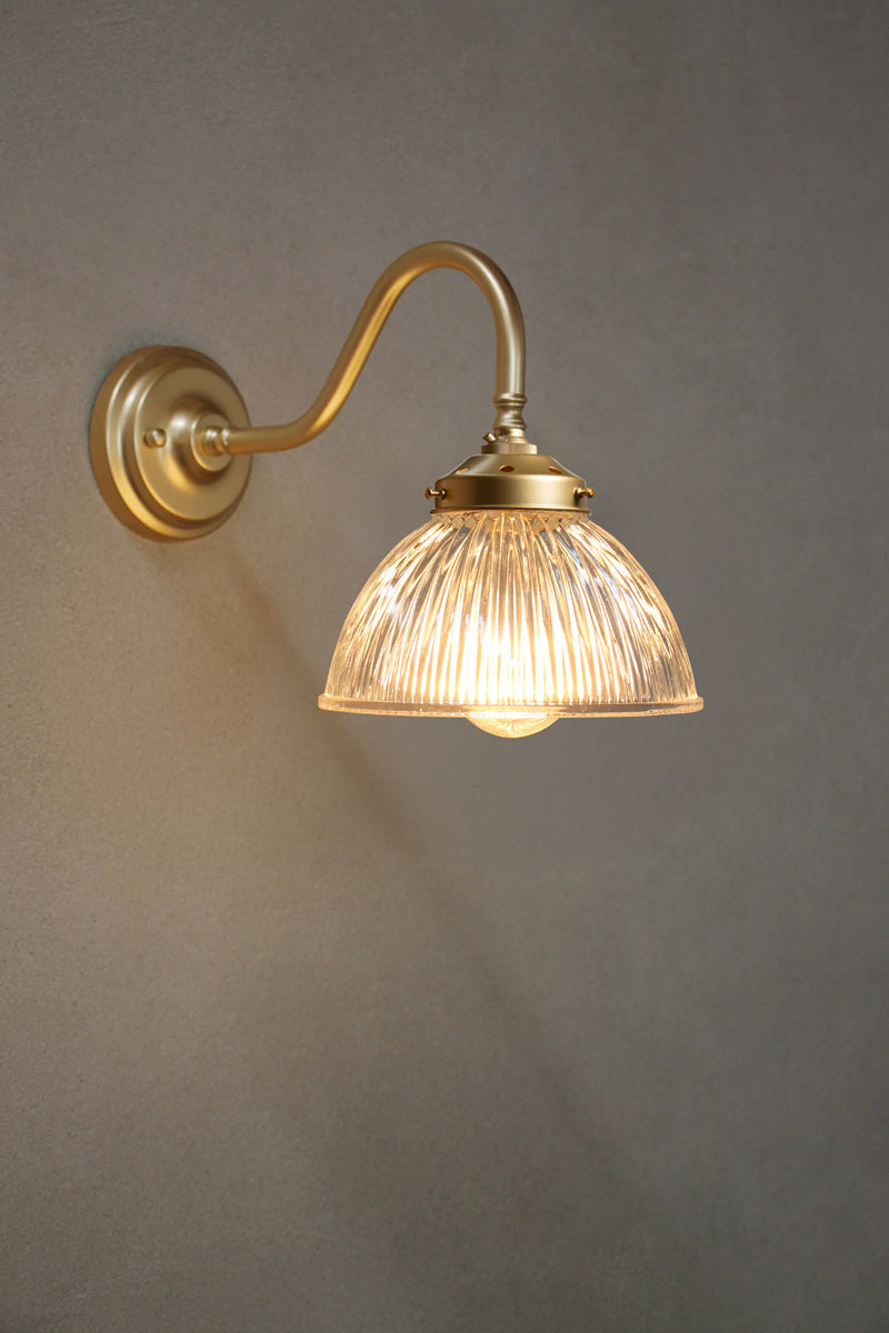 Gold wall sconce with a glass shade on a gray wall