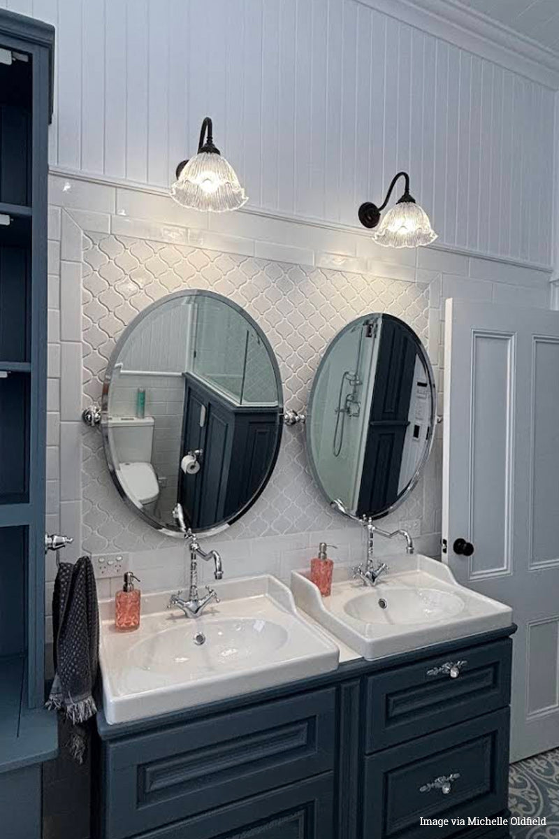 Bathroom with double sink vanity, round mirrors, and glass como frill wall lights.