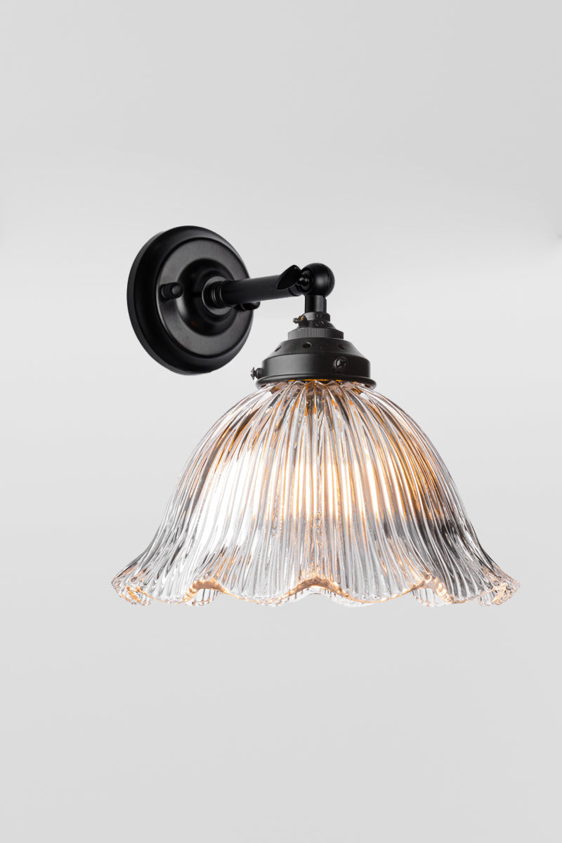 Short arm wall sconce in black with a clear holophane shade with a frilled edge. 