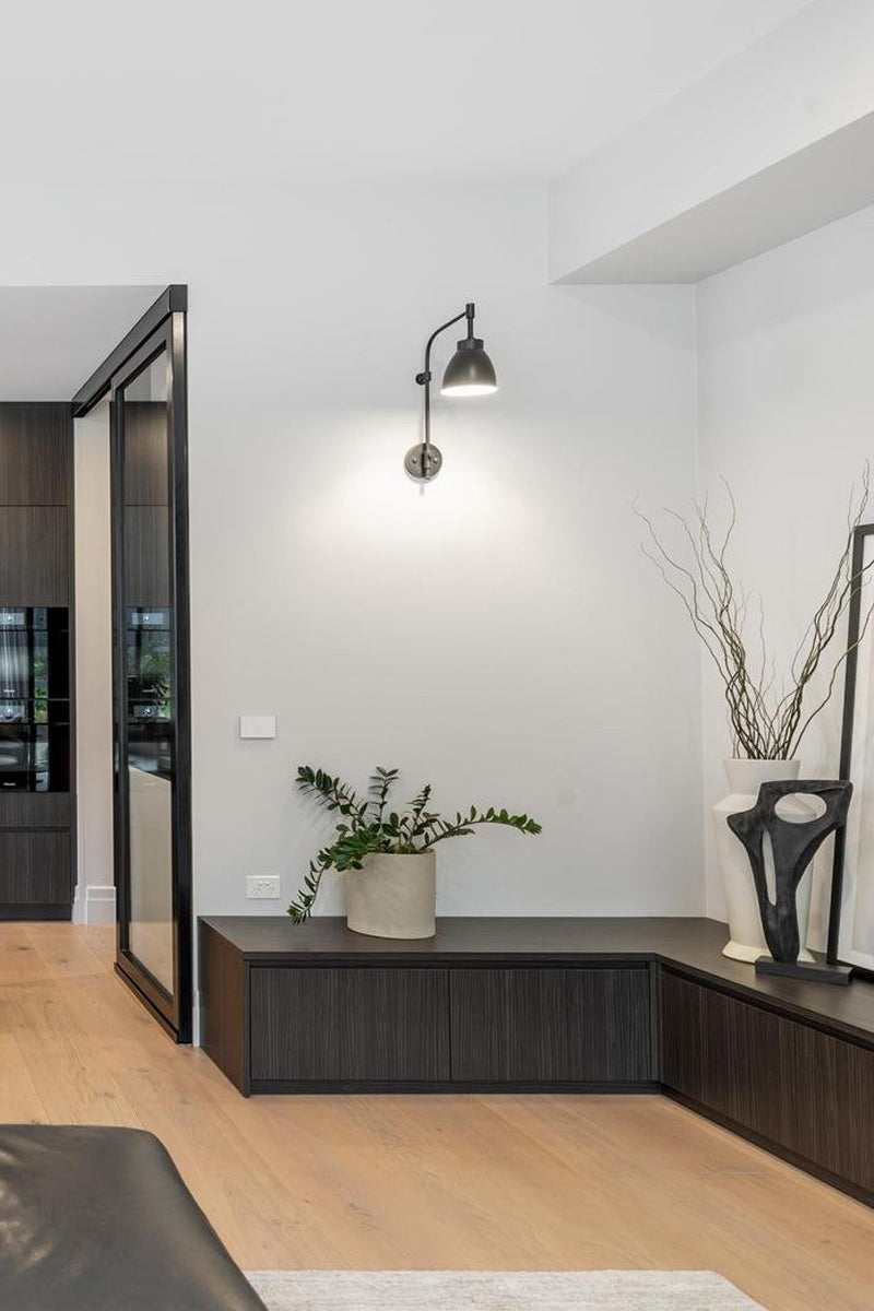 Black wing arm wall scone with black metal shade in a modern lounge corner. 