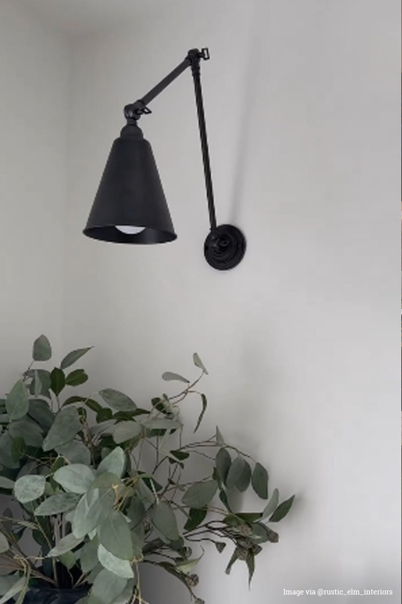 An antique bronze cone shade swing arm wall light hanging above a vase of greenery.